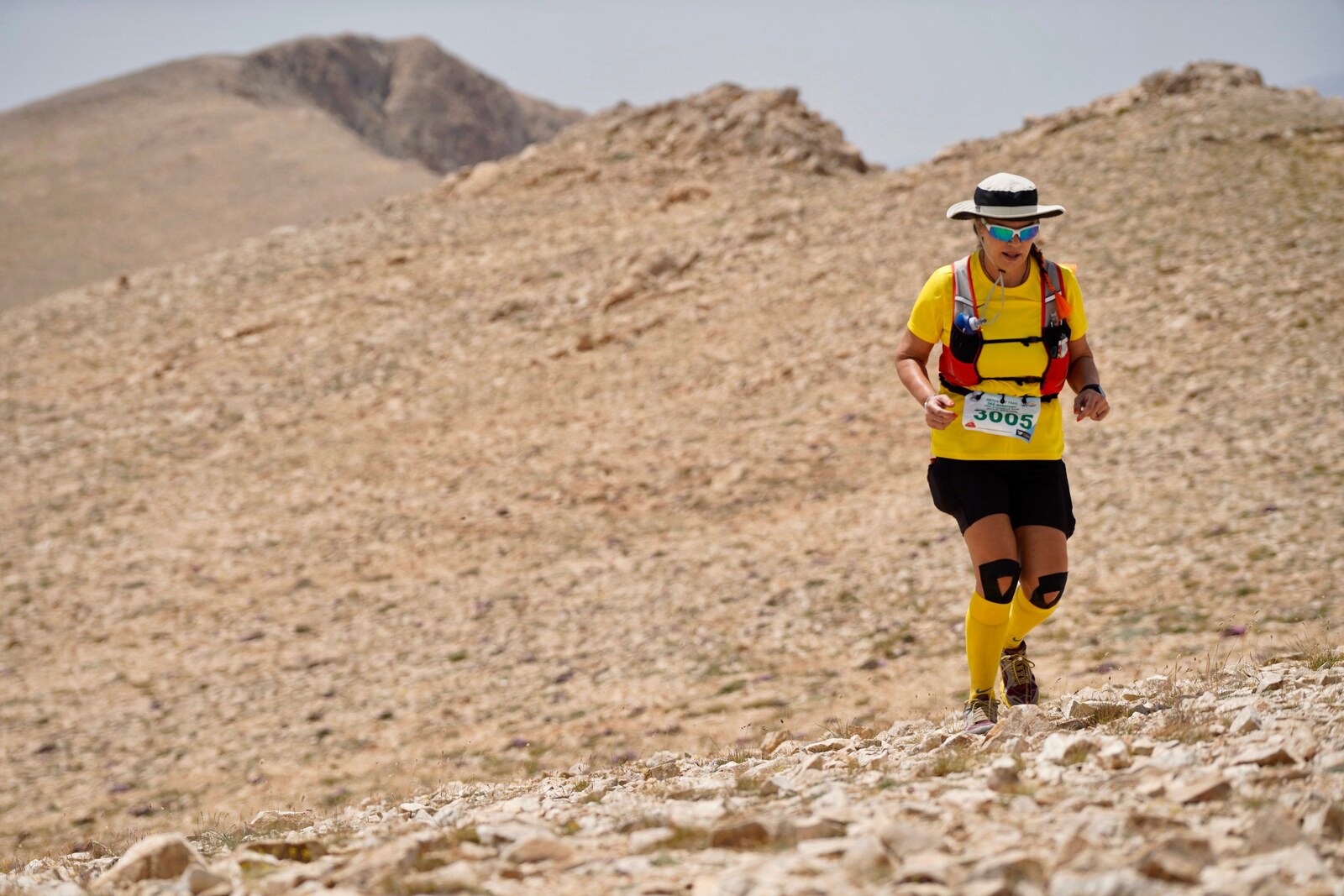 Traileuse en tenue jaune courant sur un sentier rocheux en montagne